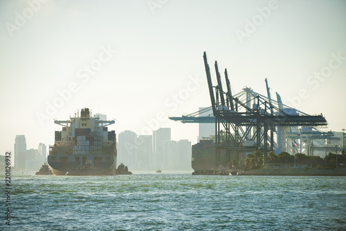 Large container ship being brought into port by tug boats with skyscraper city skyline backdrop photo