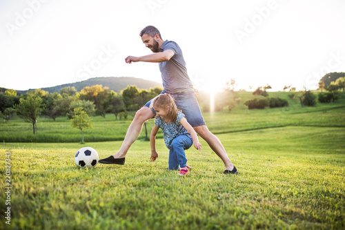 Father with a small daughter playing with a ball in spring nature at sunset.