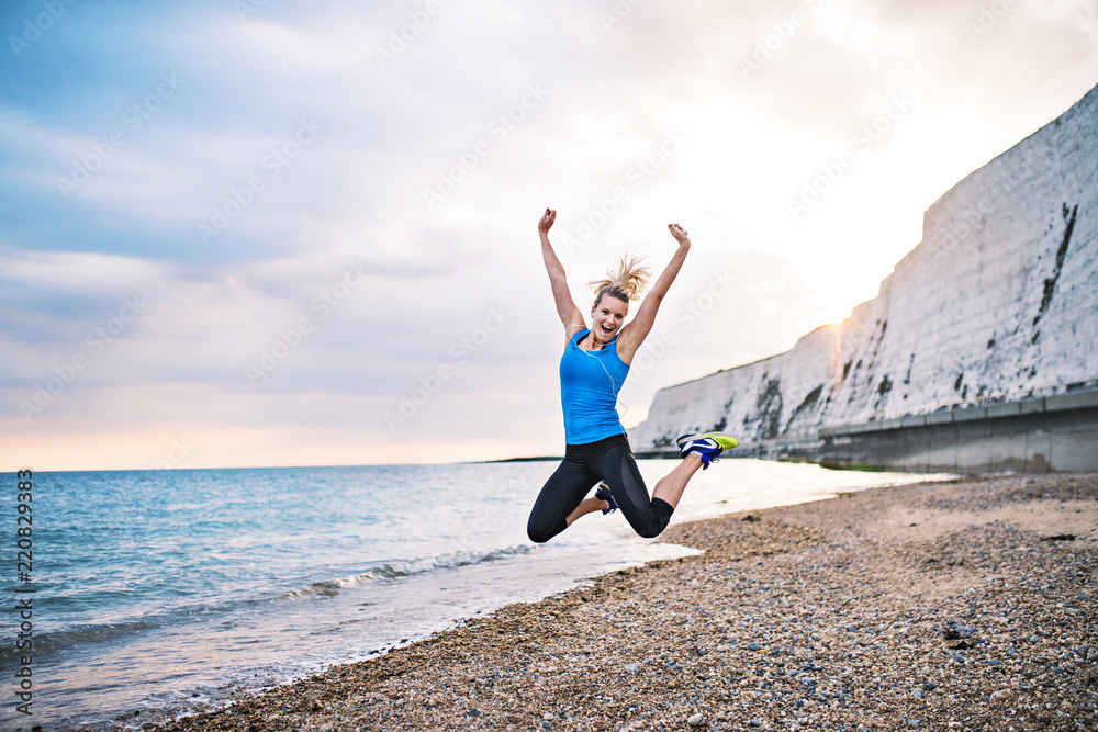 Young sporty woman runner in blue sportswear jumping on the beach outside. Young sporty woman runner in blue sportswear jumping on the beach outside.