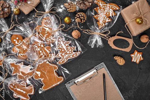 Billede på lærred A Christmas gingerbread cookie in the shape of a Christmas tree in a cellophane packing on the background of a dark table
