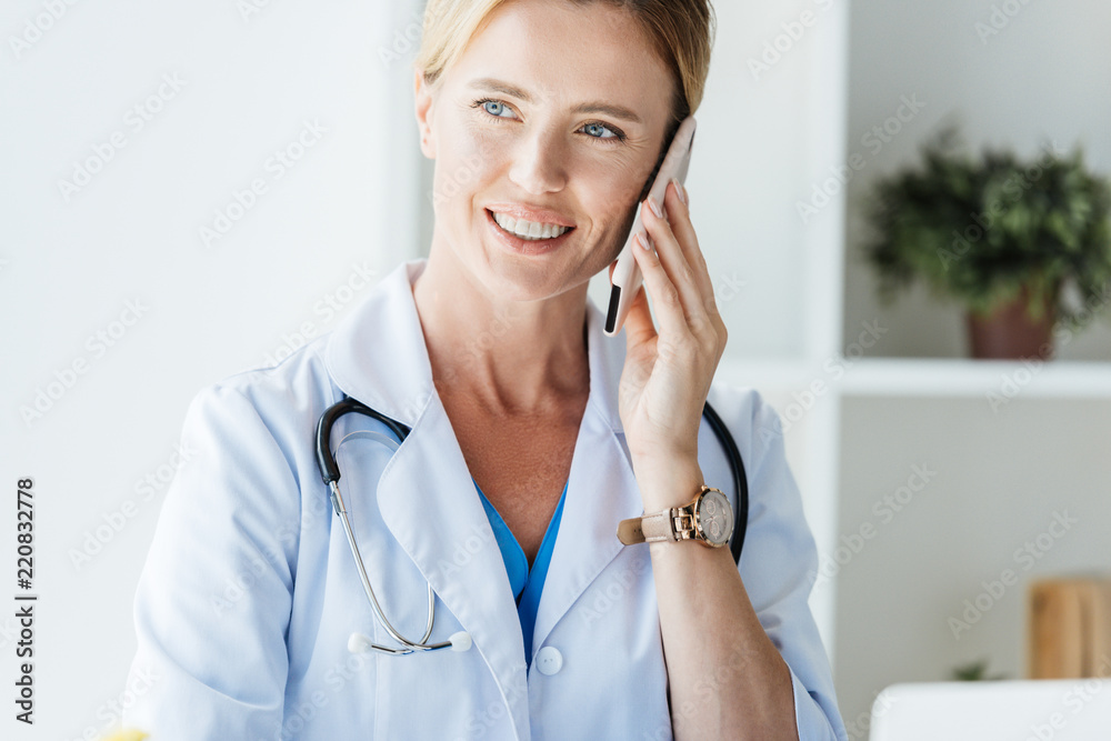 portrait of female doctor in white coat looking away and talking on smartphone in office portrait of female doctor in white coat looking away and talking on smartphone in office