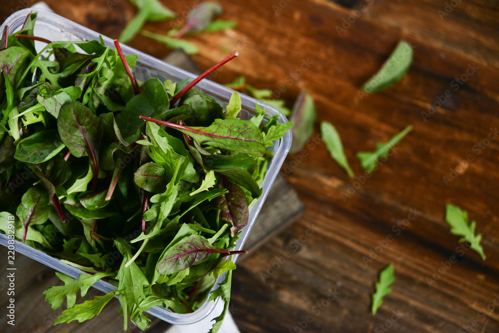 Fresh Greens Salad In a Plastic Box on wooden background: Salad Mix, Arugula, chard, Misun. The Concept Of Fast And Healthy Food, Organic Food, Vegetarianism. Fresh Greens Salad In a Plastic Box on wooden background: Salad Mix, Arugula, chard, Misun. The Concept Of Fast And Healthy Food, Organic Food, Vegetarianism.