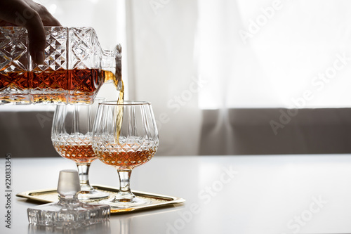 Frau schenkt Weinbrand aus Kristallflasche in Bleikristall Schwenker Gläser auf Metall Tablett und trinkt photo
