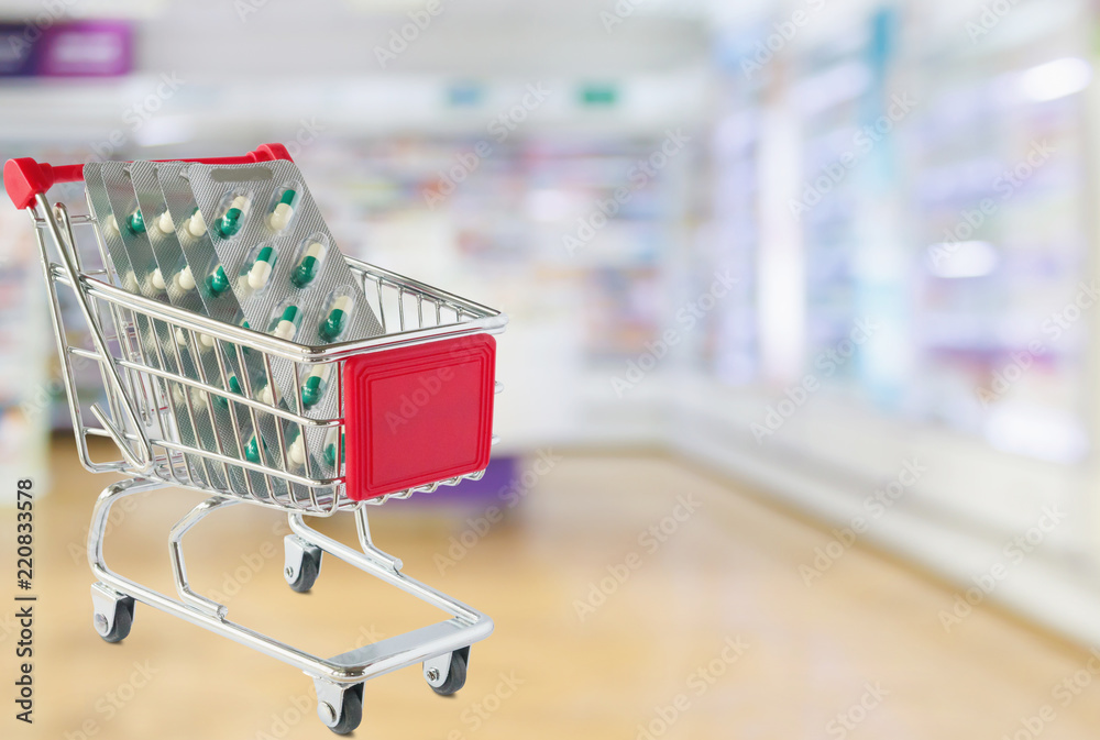 Medical pills capsule in shopping cart with pharmacy drugstore shelves blurred background