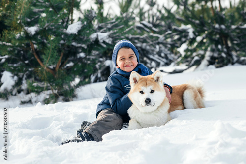 Little child and mom plays with funny Akita-inu dog in a winter park. Christmas happy family,mother and son walking with dog lying on snow in winter day. Drinking hot coffee or tea on snowy winter