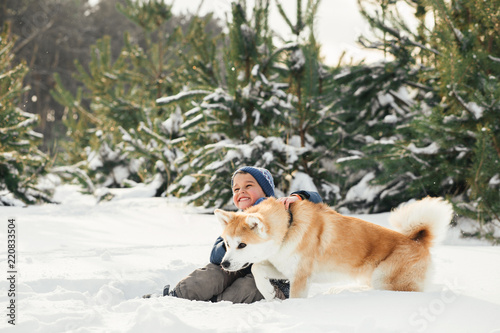 Little child and mom plays with funny Akita-inu dog in a winter park. Christmas happy family,mother and son walking with dog lying on snow in winter day. Drinking hot coffee or tea on snowy winter