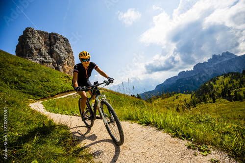 Woman cycling in Cortina d'Ampezzo, stunning Cinque Torri and Tofana in background. Riding MTB trail. South Tyrol province of Italy, Dolomites. © Gorilla