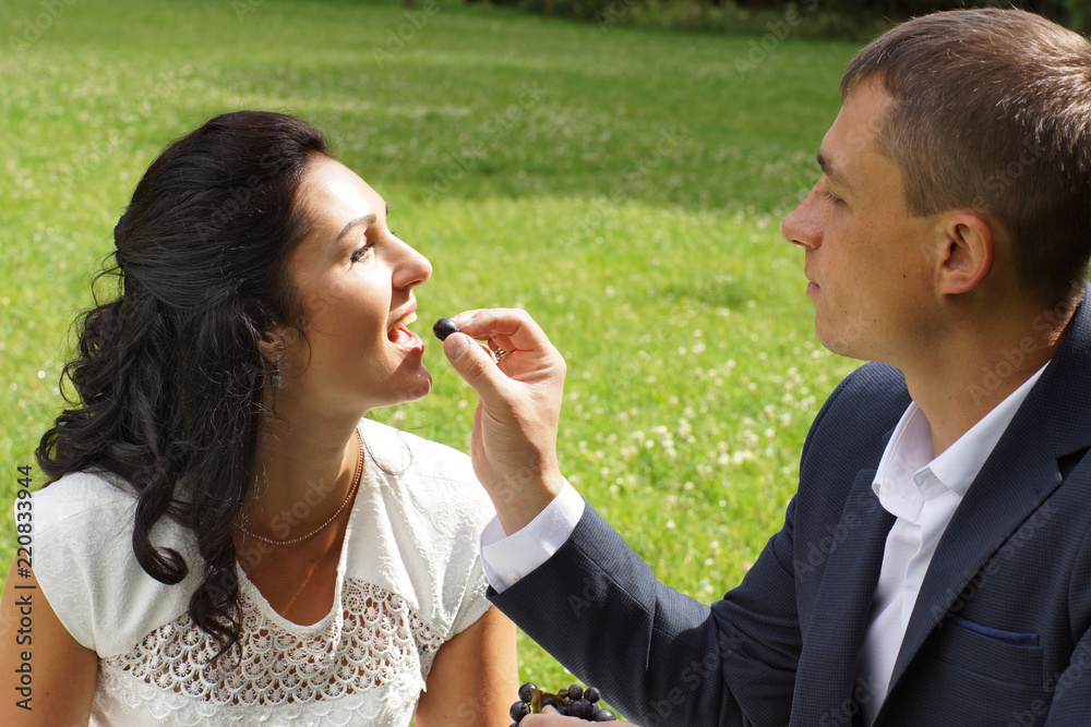 Fototapeta premium A young man is feeding his bride with grapes on a picnic in the park