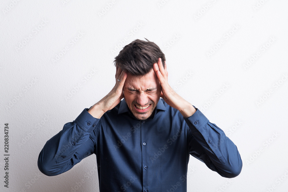 Portrait of a young man with headache in a studio, holding his head. Portrait of a young man with headache in a studio, holding his head.