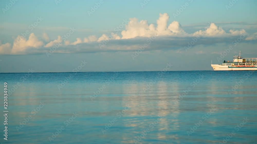 The ship swims along the horizon into the sea, in the early morning clouds and the ship are reflected in the water The ship swims along the horizon into the sea, in the early morning clouds and the ship are reflected in the water