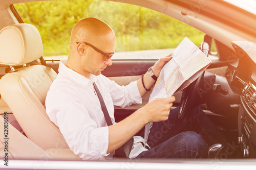 Man traveler in car looking at a paper map. Guy searching for place to go on a map. Closeup, vibrant warm colored image, no retouch, natural lighting.