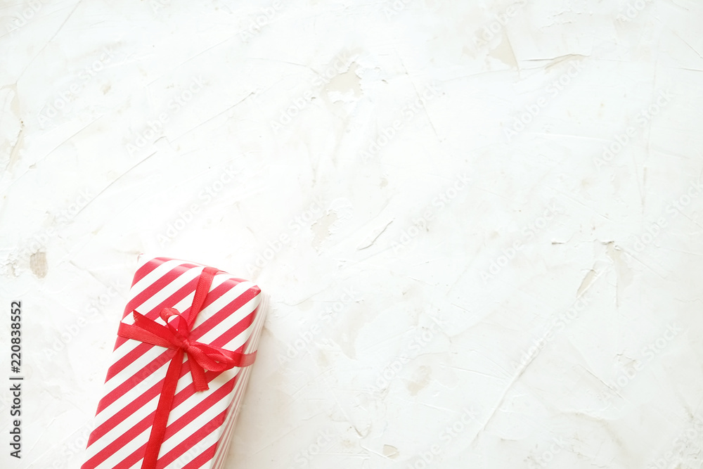 Christmas and new year present wrapped in festive colorful red and white stripe pattern paper. Single holiday gift box on white concrete texture table. Close up, background, copy space, top view. Christmas and new year present wrapped in festive colorful red and white stripe pattern paper. Single holiday gift box on white concrete texture table. Close up, background, copy space, top view.
