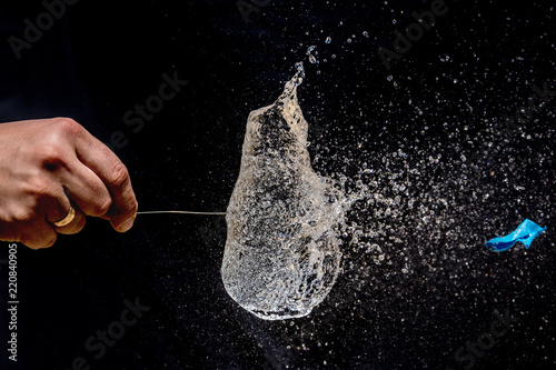 Bursting of a blue balloon filled with water with a long pin on black background. 