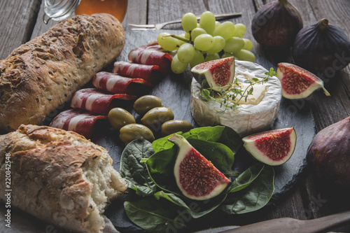 camembert cheese, figs, jamon ,honey and homemade bread, on dark serving board over rustic wooden background