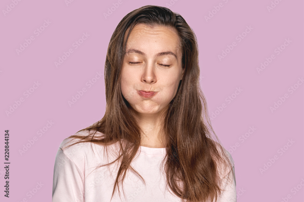 Funny pretty girl puffing out her cheeks against lavender studio background. Headshot of charming red haired young woman making mouths while having fun indoors. People, lifestyle, youth and happiness Funny pretty girl puffing out her cheeks against lavender studio background. Headshot of charming red haired young woman making mouths while having fun indoors. People, lifestyle, youth and happiness