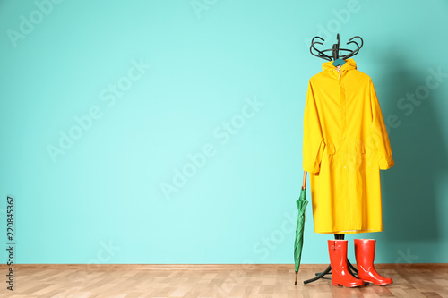 Umbrella, rain coat and boots near color wall with space for design