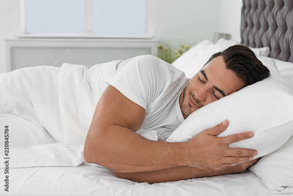 Young man sleeping in bed with soft pillows at home
