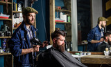 Bearded man getting groomed at hairdresser with hair dryer while sitting in chair at barbershop. Hipster concept. Hipster bearded client getting hairstyle. Barber with hairdryer drying hair of client