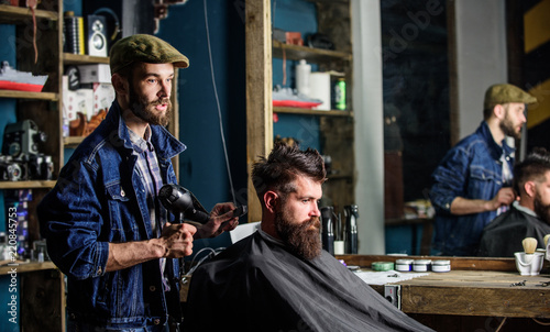 Bearded man getting groomed at hairdresser with hair dryer while sitting in chair at barbershop. Hipster concept. Hipster bearded client getting hairstyle. Barber with hairdryer drying hair of client © be free