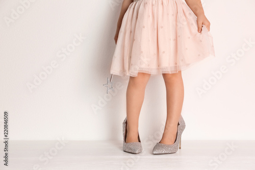 Little girl in oversized shoes near white wall with space for text, closeup on legs