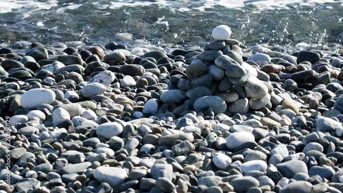 Pebble sea beach and a pyramid of small stones on the edge of the surf as entertainment for vacationers
 photo