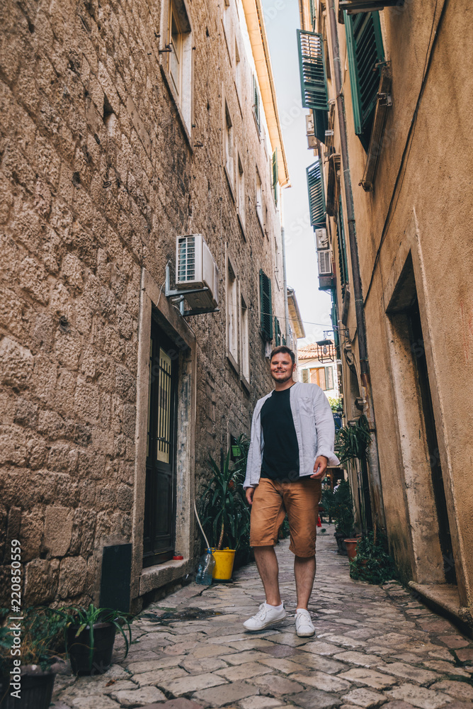 young stylish man walking by tight Kotor street. Montenegro