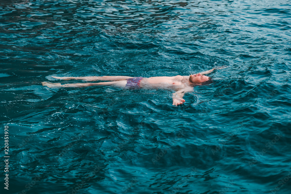 man swimming on back in blue transparent sea water