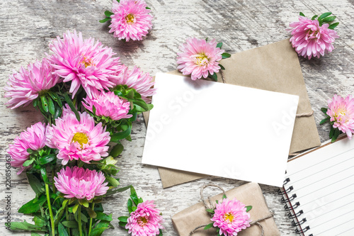 Creative layout made with pink aster flowers  blank greeting card  notepad and gift box on white wooden background