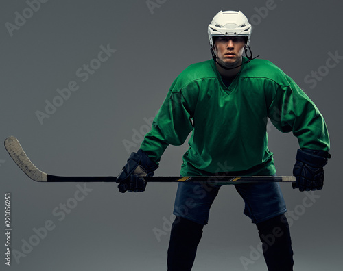 Photography Portrait of a professional hockey player wearing full gear and a hockey stick on a gray background