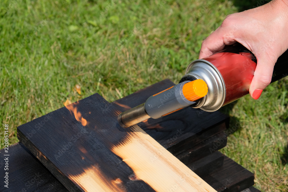 a woman's hand with a gas burner in her hand. burns a wooden board