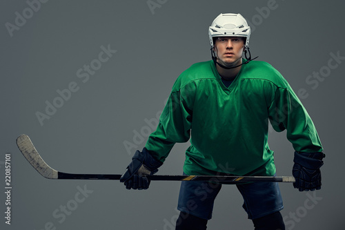 Portrait of a professional hockey player wearing full gear and a hockey stick on a gray background.