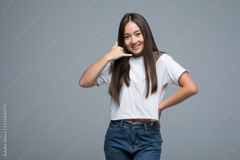 Call me, please. Portrait of young, cute, smiling asian girl in white t-shirt gesturing smart phone with one hand standing over grey background