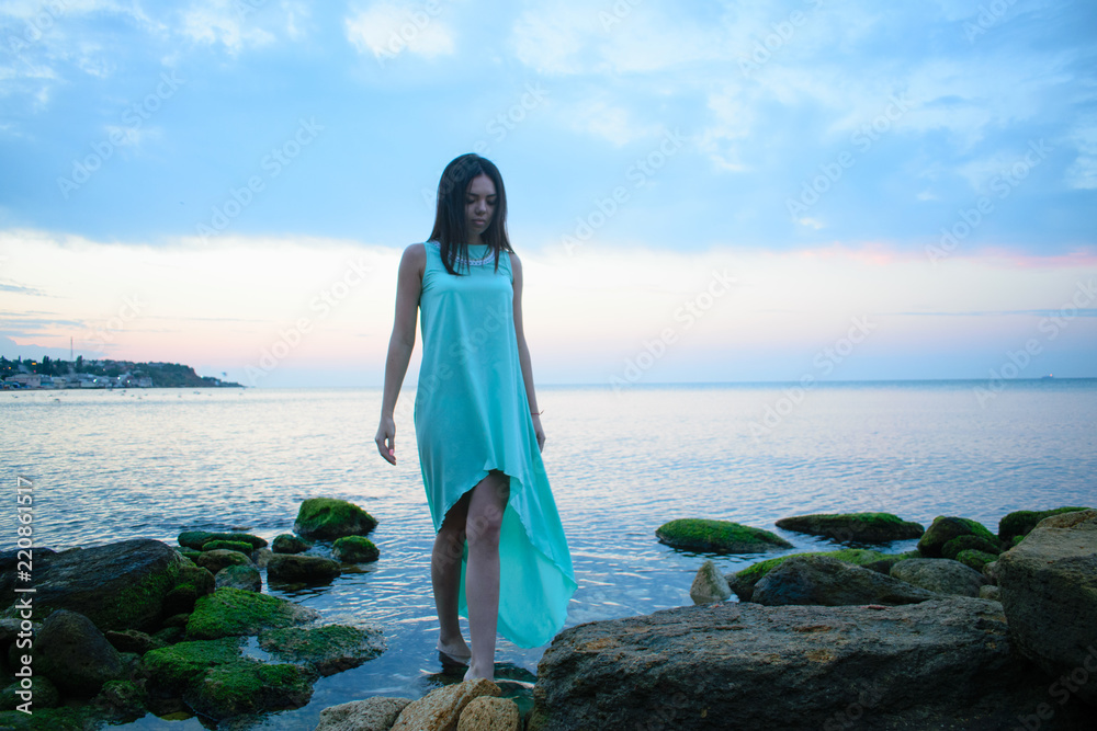 beautiful girl in blue dress on the waterfront on a sunset background, dawn. beautiful girl in blue dress on the waterfront on a sunset background, dawn.