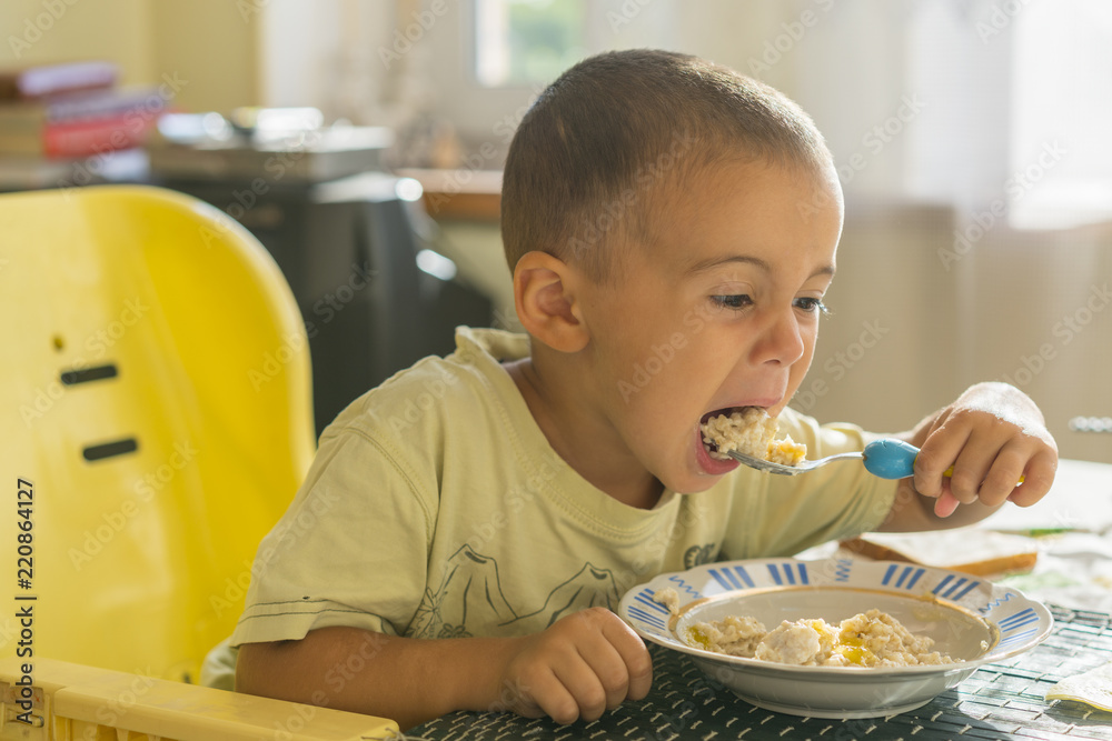 The boy 2 years eats porridge. Children's table. The concept of the child's independence. happy little boy eating porridge. Little boy eating breakfast at the table The boy 2 years eats porridge. Children's table. The concept of the child's independence. happy little boy eating porridge. Little boy eating breakfast at the table