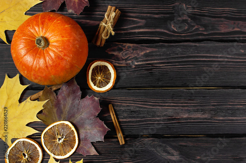 Orange pumpkin, cinnamon, slices of dried orange, autumn colorful leaves and checkered plaid on a dark wooden background top view with space for text. Autumn Pumpkin Thanksgiving Background.