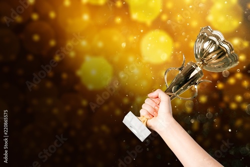 Close-up human hand holding golden Trophy on blurred background