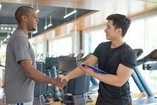 Smiling black man thanking personal trainer in gym. Young guy greeting instructor with gym equipment in background. Personal trainer concept. photo