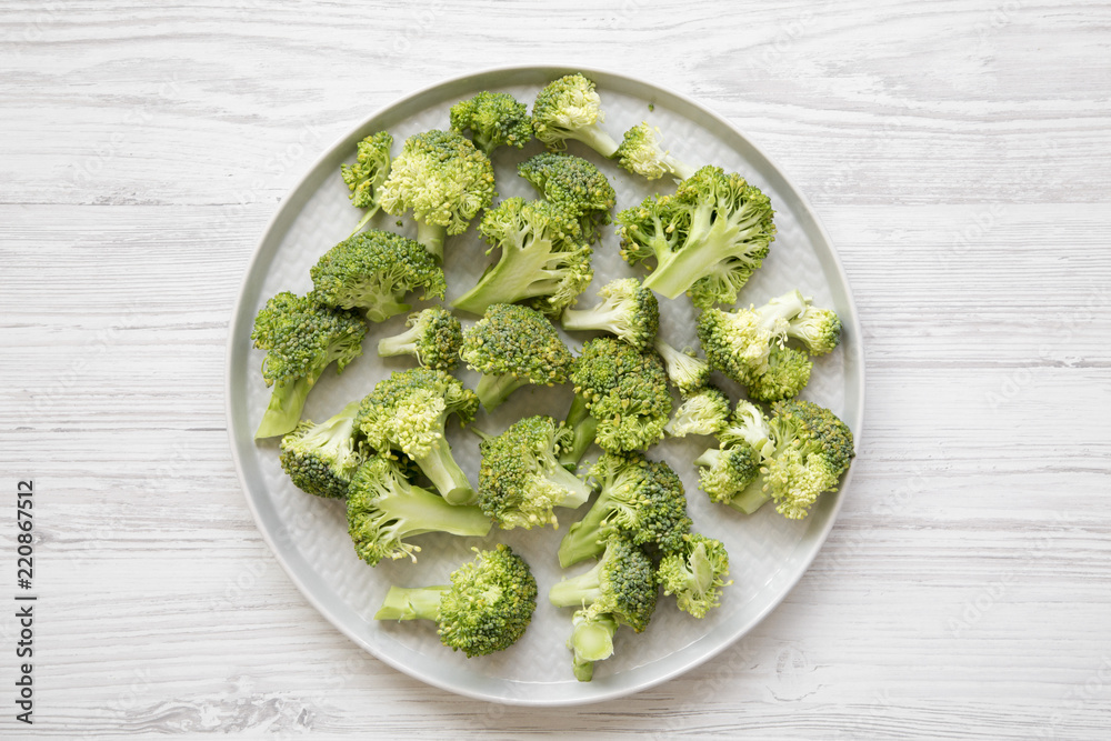 Freshly cut raw broccoli on gray plate over white wooden surface, overhead view. Flat lay, from above, top view. Freshly cut raw broccoli on gray plate over white wooden surface, overhead view. Flat lay, from above, top view.