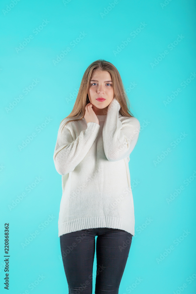 Pretty female with long hair, dressed casually in ivory sweater, looking with satisfaction at camera. Studio shot of good-looking beautiful woman isolated against blank turquoise studio wall. Pretty female with long hair, dressed casually in ivory sweater, looking with satisfaction at camera. Studio shot of good-looking beautiful woman isolated against blank turquoise studio wall.