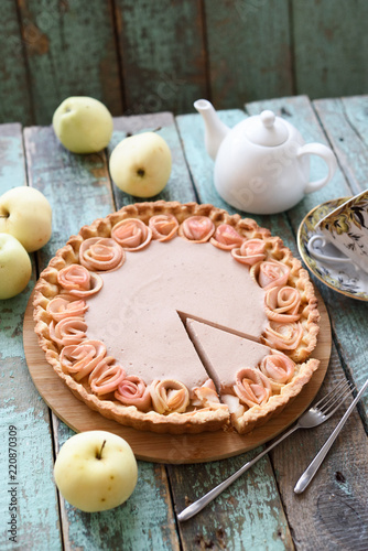 Apple rose pie with cream filling served with organic apples and tea on coarse wood blue background