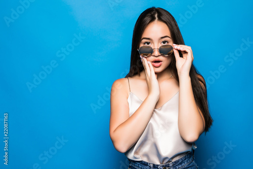 Young Asian woman with surprise pose isolated on blue background. Portrait of beautiful Asian woman with sunglasses posing surprise gesture for shock, freak, fear, fright concepts.
