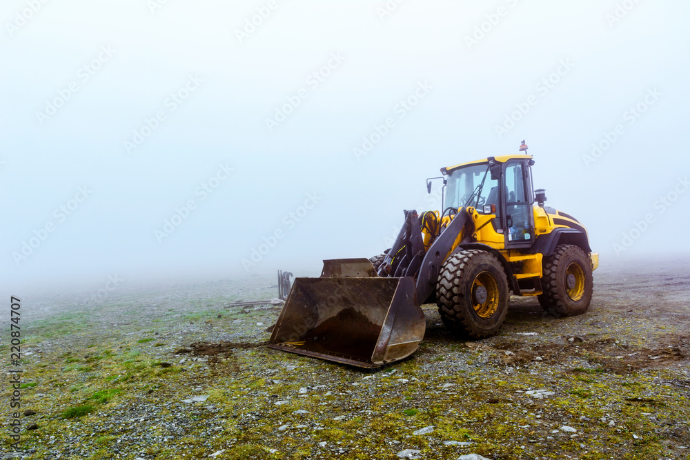 The yellow bulldozer on pale green ground in fog The yellow bulldozer on pale green ground in fog