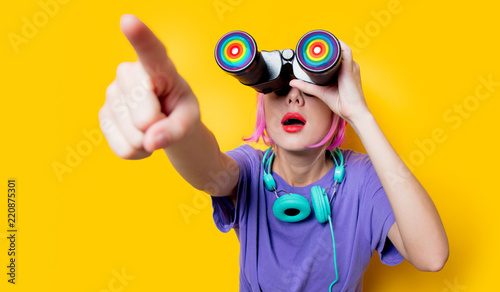 Young style girl in purple clothes with LGBT binoculars on yellow background. Clothes in 1980s style