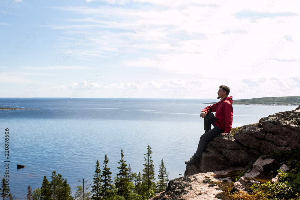 Young bearded guy in tourist clothes looking out into the distance against a blue lake