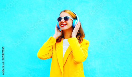 Portrait happy smiling woman listens to music in headphones on blue background