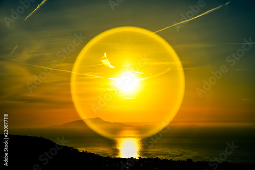 Efecto circular de luz del sol sobre el lente durante un atardecer en las costas de Sorrento al sur de Italia. Cielo de tonos naranjas y azules y monte Vesubio de fondo.  photo