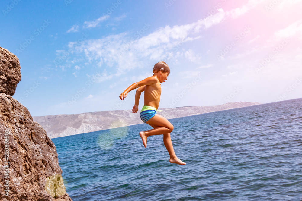 A boy is jumping from the cliff into the sea on a hot summer day. Holidays on the beach. The concept of active tourism and recreation