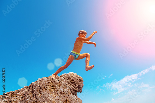 A boy is jumping from the cliff into the sea on a hot summer day. Holidays on the beach. The concept of active tourism and recreation