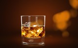 Glass of whiskey and Ice on wooden table on blurred background