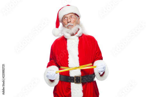 Christmas. Santa Claus is measuring waist with a tape. The concept of weight loss, healthy eating. Isolated on white background.